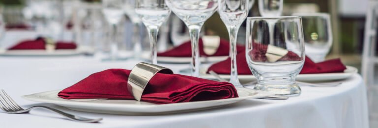 Corporate hospitality table setting. Wine glasses, plates, and red napkins.